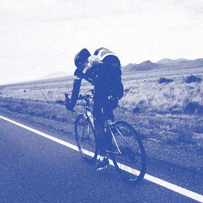 A single rider pedals on the road across a wide open plain.