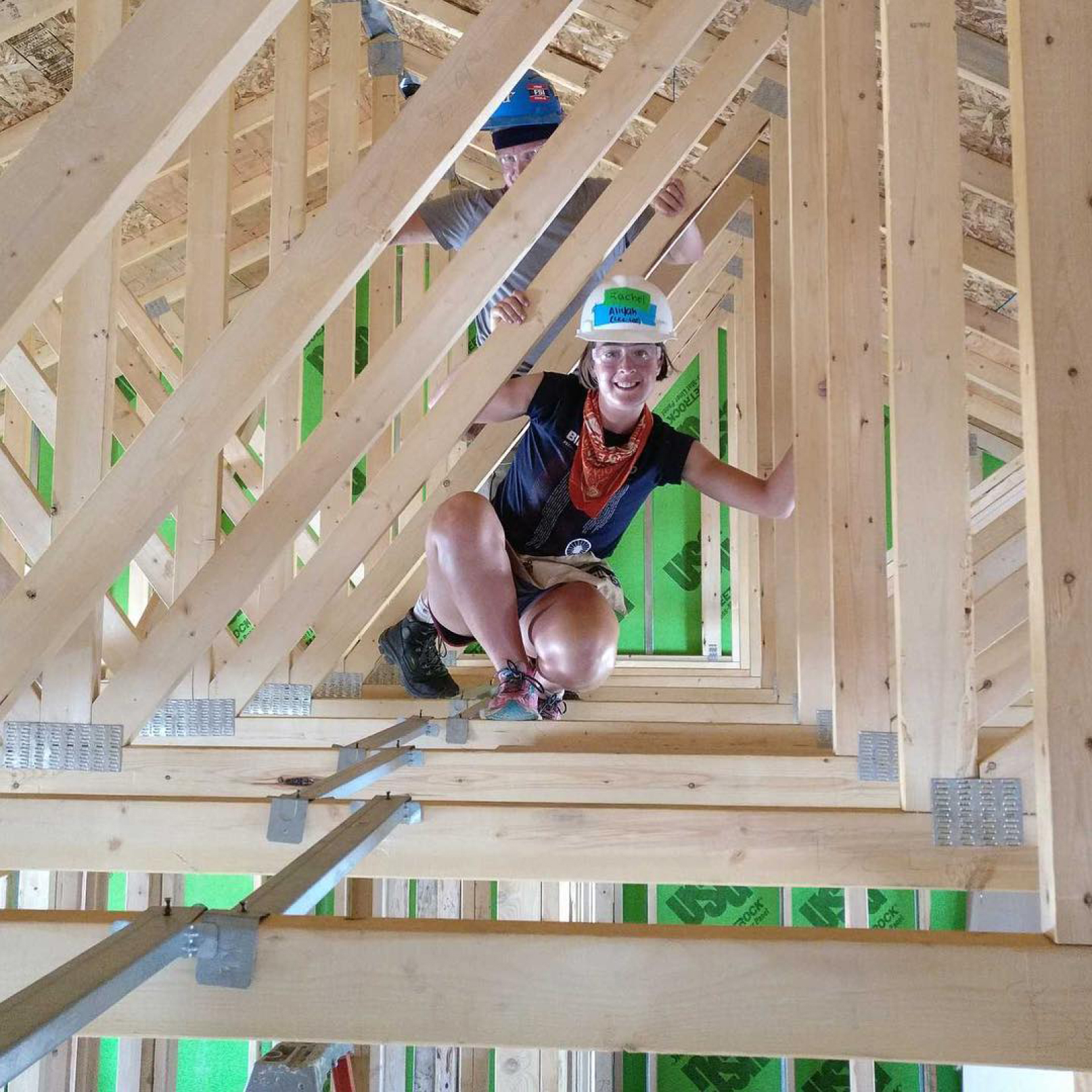 A volunteer smiling while working in the rafters of a habitat build site.