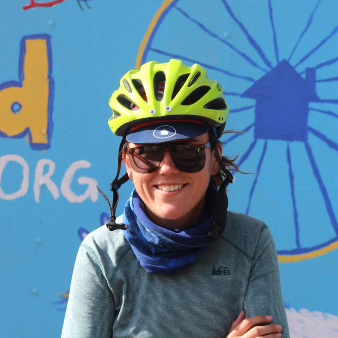 A portrait of Casey, wearing sunglasses and a bike helmet.