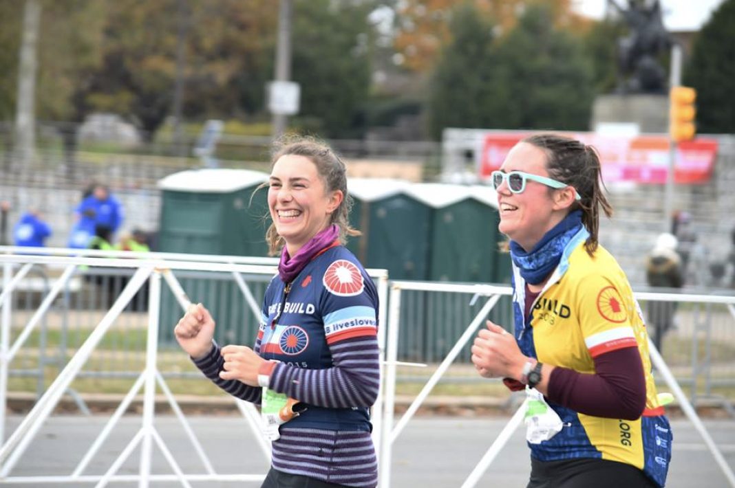 A portrait of Lily and Casey running and smiling in Bike & Build jerseys during the Philadelphia Marathon.